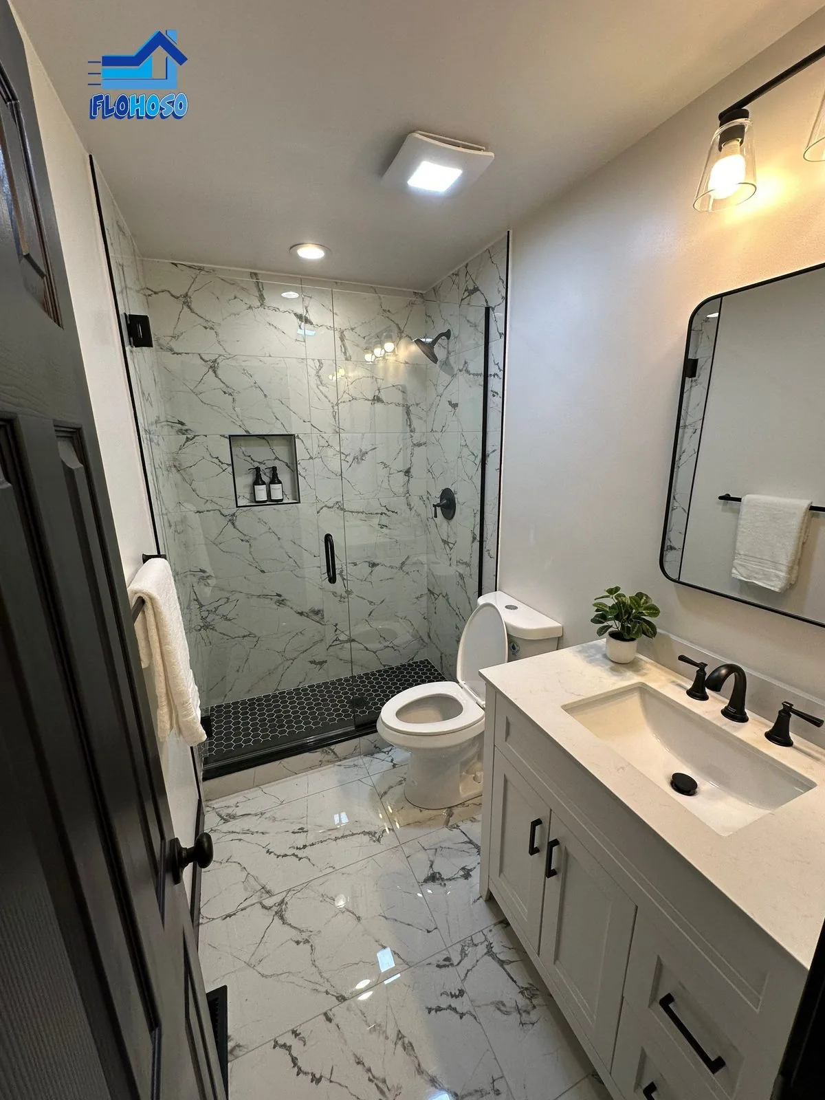 Bright bathroom with marble tile floor and walls, a glass shower enclosure and a white vanity