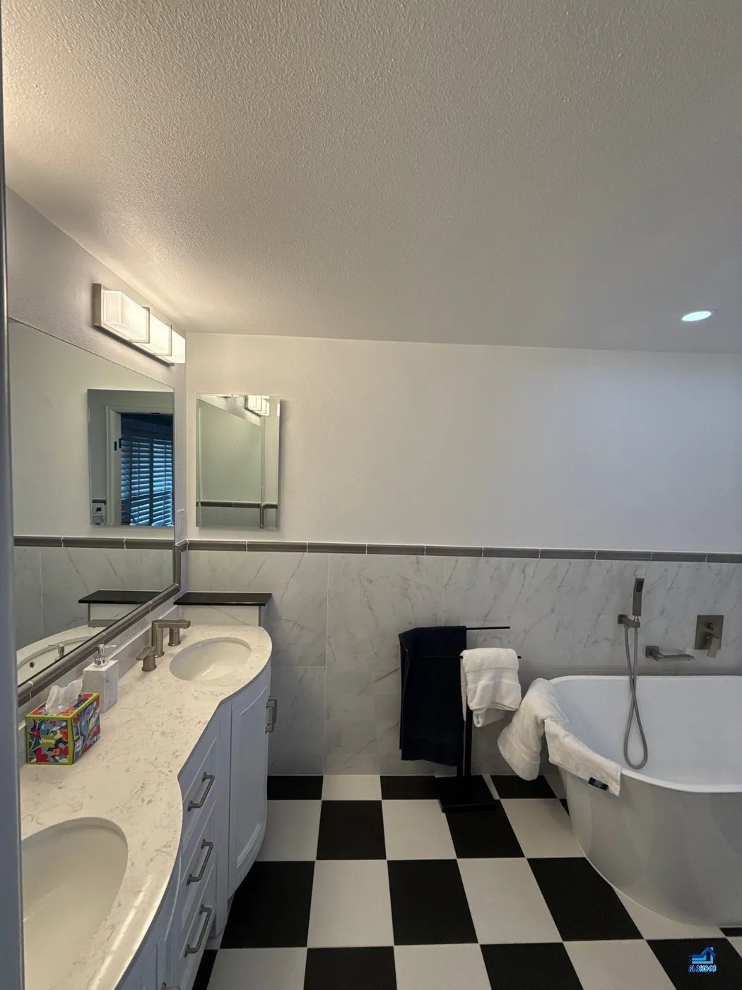 Bathroom vanity mirror reflecting a freestanding tub, marble tile wainscot and a black-and-white checkerboard floor