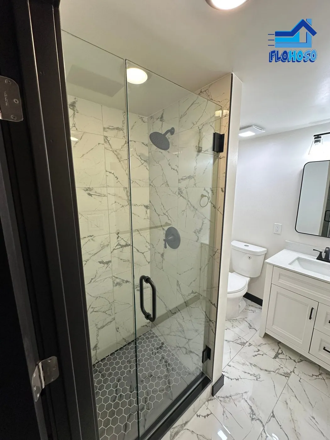 Close view of a marble-tiled shower stall with black hardware and a black hexagon mosaic floor