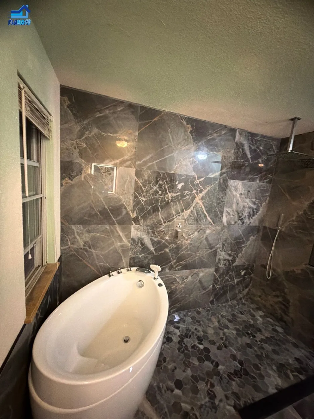 Dark stone-tiled walk-in shower with a ceiling-mount rain shower head and hexagon mosaic floor