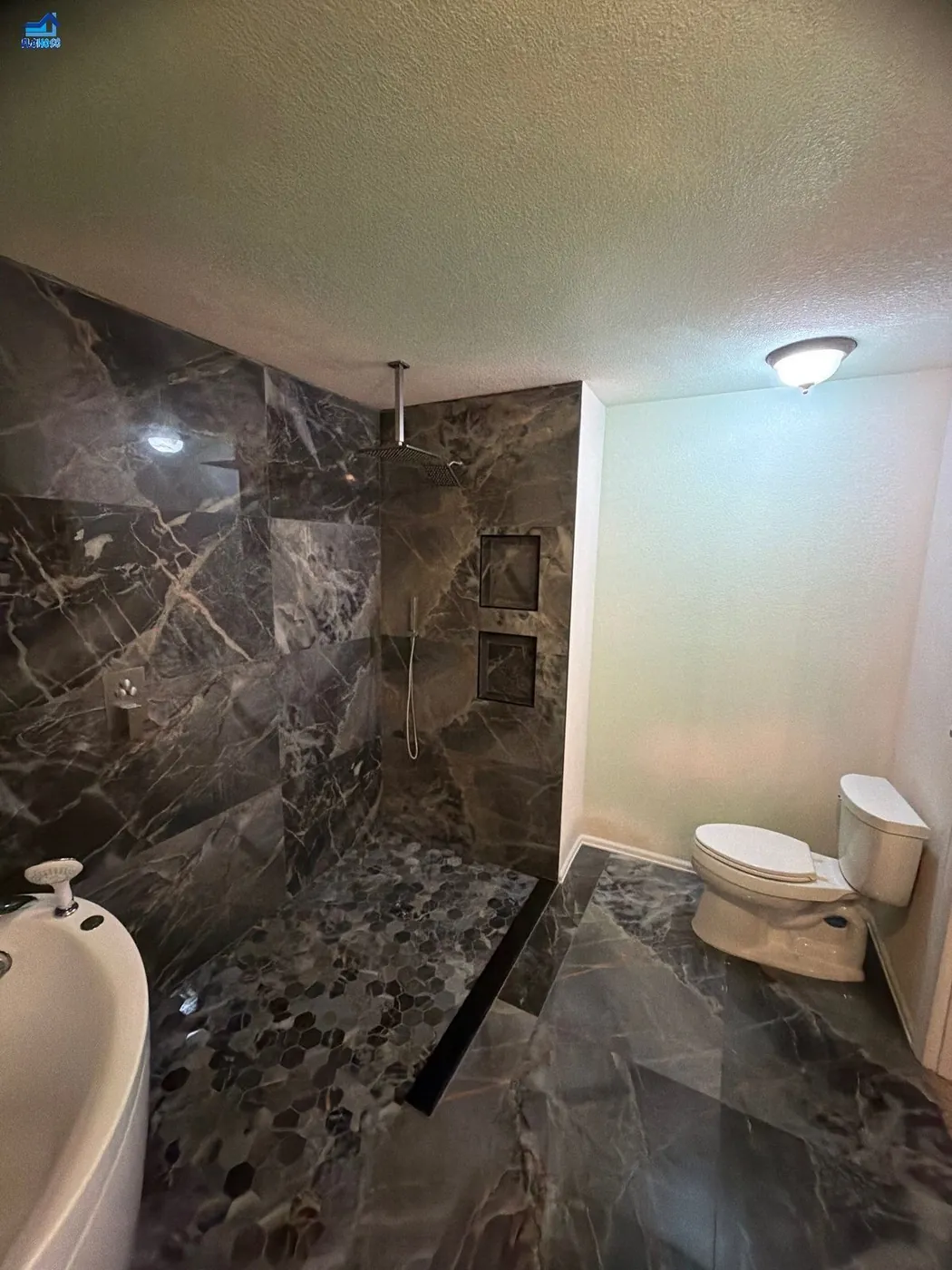 Dark stone-tiled bathroom with a walk-in shower, rain shower head and matching stone floor